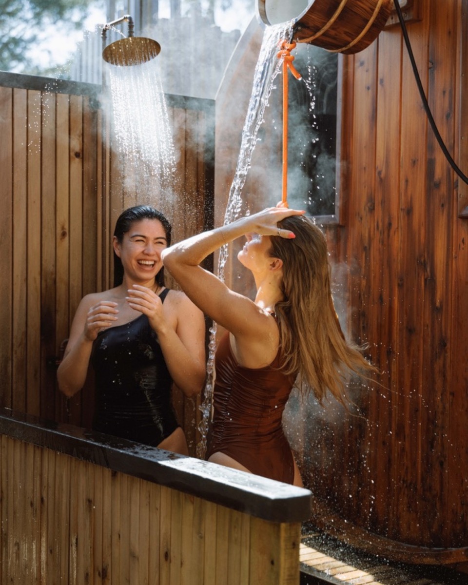 Two friends laughing in an outdoor cedar sauna and rain shower