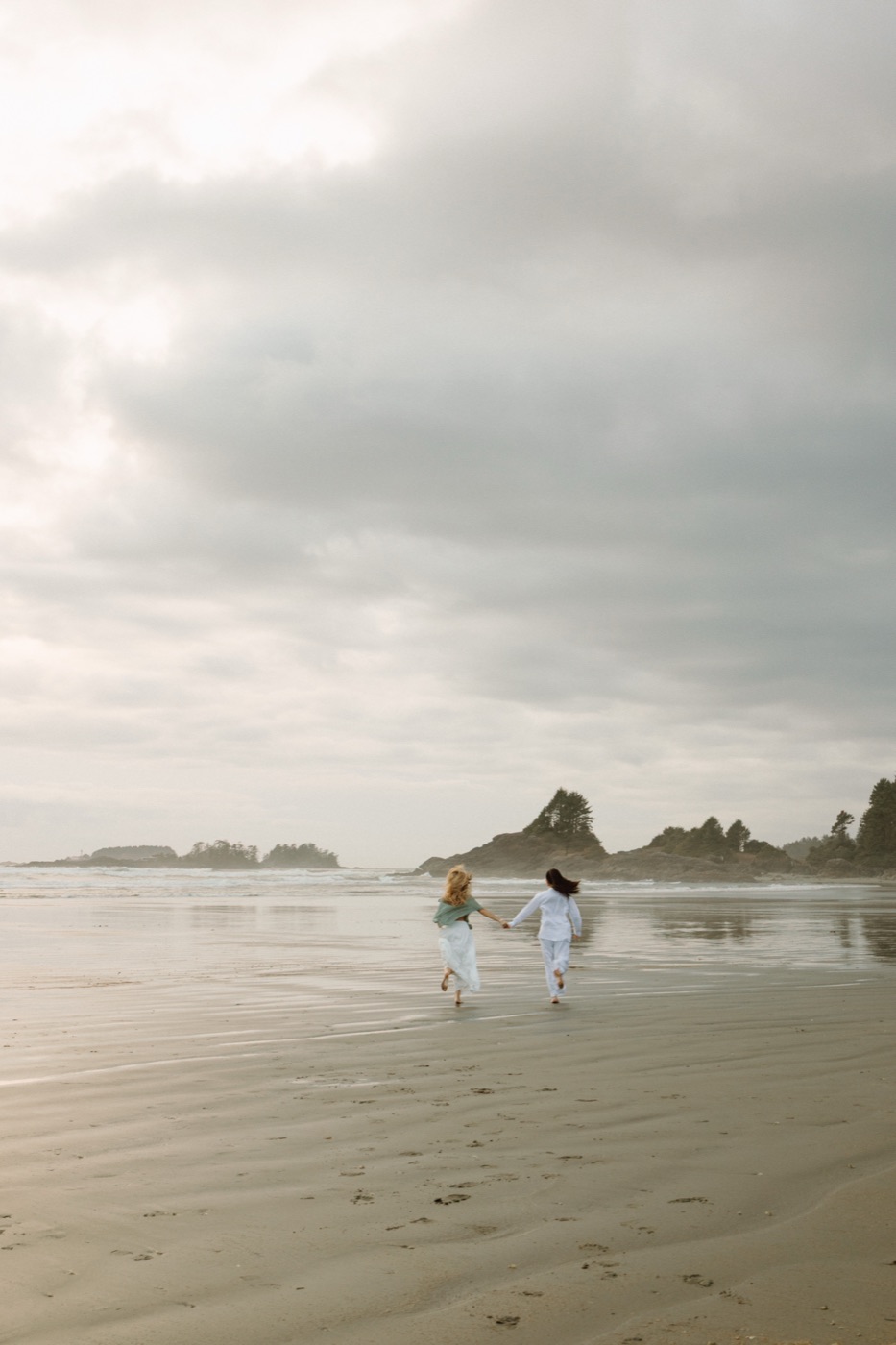 Two people walking on a misty Tofino, BC Canada beach at dawn